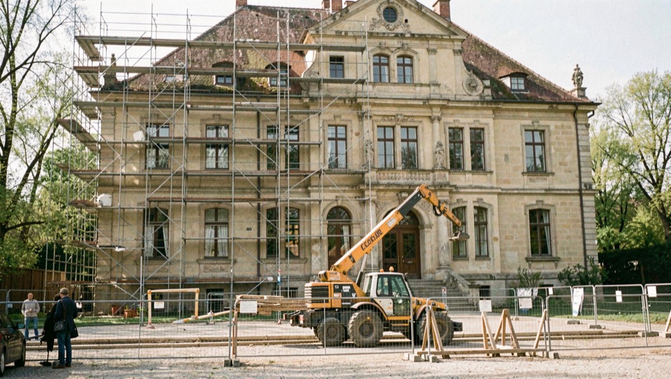 Altes Herrenhaus mit Baugerüst: Kipplader und Bauzaun vor der historischen Fassade im Frühjahrslicht